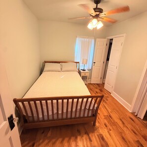 A bedroom with a wooden bed, a ceiling fan, and a nightstand with a lamp. - Cozy 2-bedroom cottage in Nottoway, VA (Crewe)
