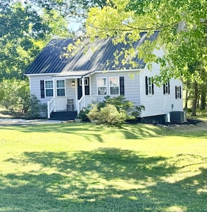 A single-story house with a porch, a front yard, and a tree in the background.