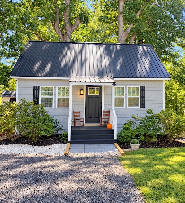 A two-story house with a dark roof, white siding, and a front porch with two chairs.