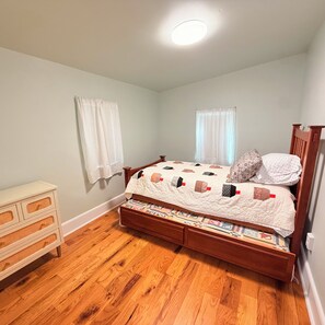 A bedroom with a wooden bed, a dresser, a window with curtains, and a ceiling light.