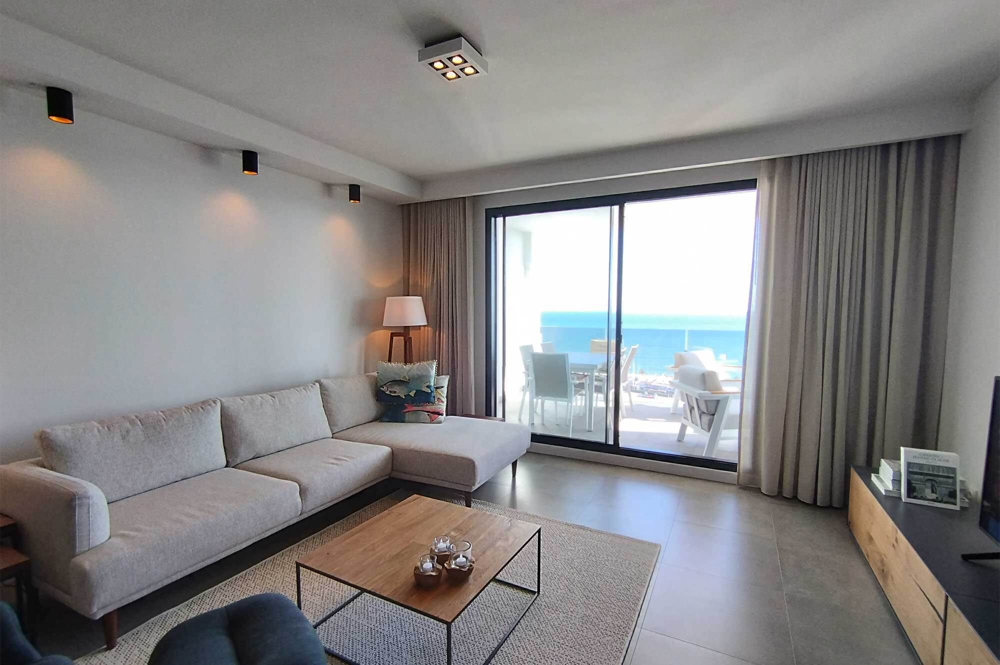 A modern living room with a sofa, a coffee table, and a view of the ocean through large windows.