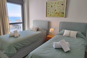 Una habitació d'hotel amb dos llits, una finestra amb cortines, un quadre a la paret i una tauleta de nit amb una làmpada.
