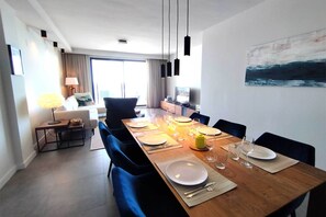 A dining area with a wooden table set for four, a TV in the background, and a painting on the wall. - Sea View Apartment in La Paloma de Manilva (Manilva)