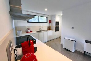 Uma cozinha moderna com armários brancos, coifa de aço inoxidável, forno embutido e uma máquina de lavar louça compacta.