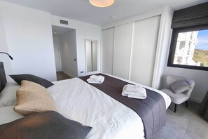 A hotel room with a bed, a chair, a window, and a door. - Sea View Apartment in Blue Suites (Manilva)
