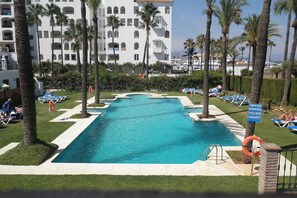 Ein Swimmingpool mit Liegestühlen und Palmen, umgeben von einem Gebäude mit mehreren Balkonen.