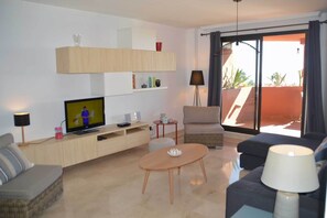 A living room with a television, sofa, armchair, and a small table. - Apartment with Sea and Golf Course Views (Casares)