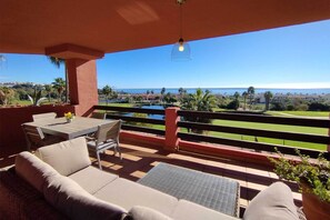 A balcony with a table and chairs, a sofa, and a view of a golf course and ocean. - Apartment with Sea and Golf Course Views (Casares)