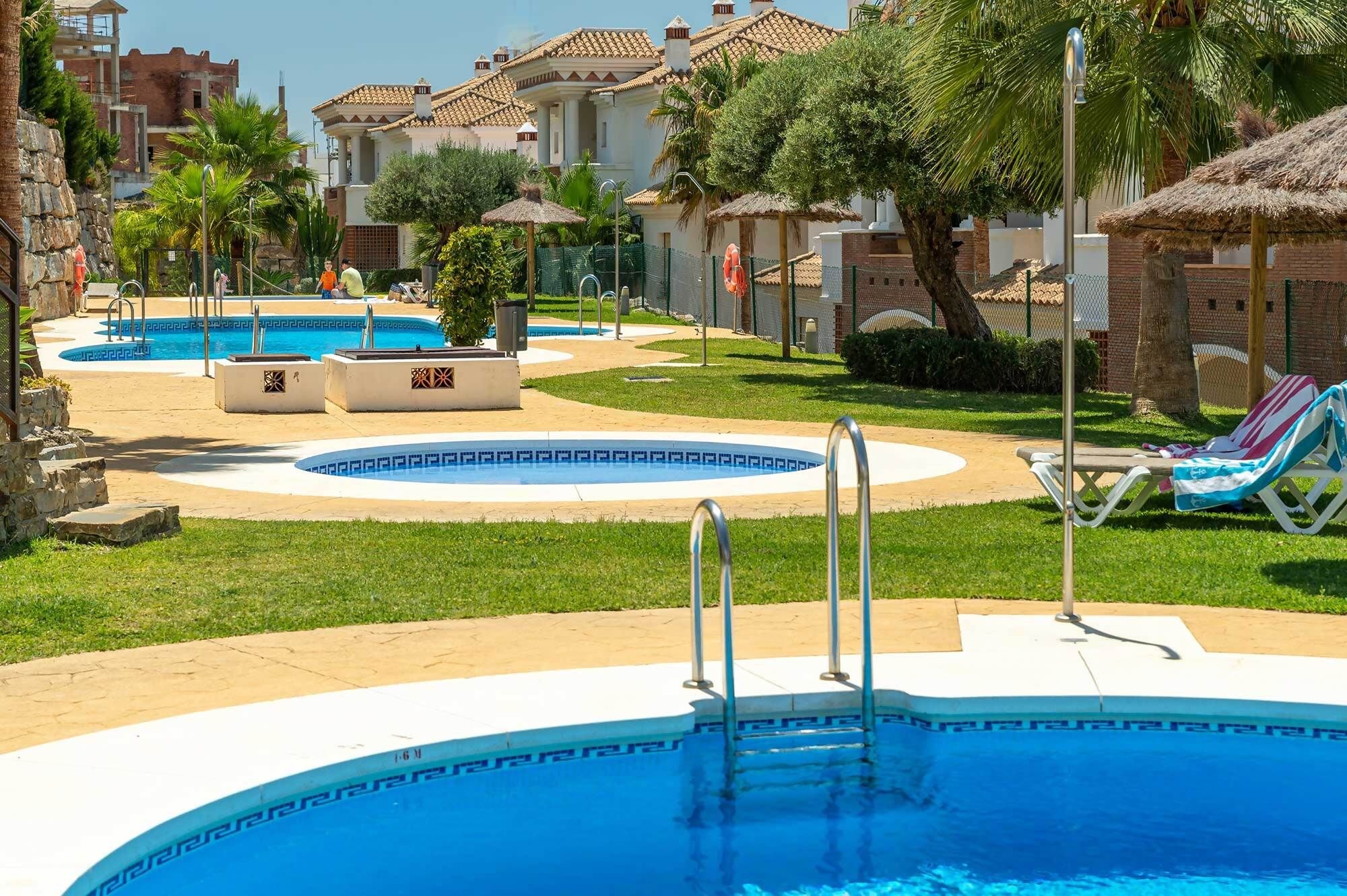 A pool area with multiple swimming pools, lounge chairs, and palm trees.