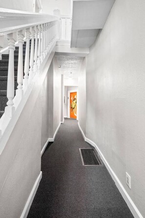 A narrow hallway with a white railing on one side and a door with an orange frame at the end. - The Platypus - Spacious 1BR, Walk to Mass Ave (Indianapolis)