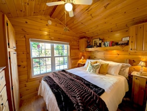 A wooden cabin bedroom with a bed, window, and ceiling fan. - Kennebec River Cabin with Barrel Sauna & Porch (Richmond)