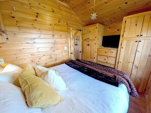 Ein Zimmer in einer Holzhütte mit einem Bett, einem Fernseher und Holzschränken.