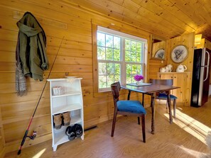 A wooden cabin interior with a dining table, chairs, a kitchen area, and a fishing rod. - Kennebec River Cabin with Barrel Sauna & Porch (Richmond)