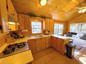 A cabin interior with a kitchen, dining area, and a bed with a window view. - Kennebec River Cabin with Barrel Sauna & Porch (Richmond)