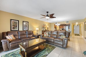 A living room with leather sofas, a coffee table, and a ceiling fan. - Reef Club 508 - Beachfront 3br/2ba luxury condo with pool and tennis (Indian Rocks Beach)