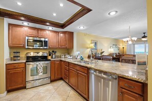 A modern kitchen with stainless steel appliances, wooden cabinets, and a granite countertop. - Reef Club 509 - Beachfront 3br/2ba luxury condo with pool and tennis (Indian Rocks Beach)
