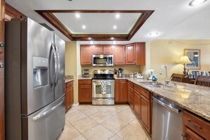 Cocina con electrodomésticos de acero inoxidable, armarios de madera, encimeras de granito y piso de baldosas.