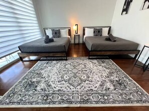 Une chambre avec deux lits, une grande moquette à motifs, une table de chevet avec une lampe et une fenêtre avec des stores.