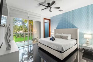 A modern hotel room with a large bed, a ceiling fan, and a view of a green outdoor area. - Fort Lauderdale Beach 8BR Modern Retreat (Fort Lauderdale)