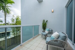 A balcony with a glass railing, two wicker chairs with cushions, a potted plant, and a large window. - Fort Lauderdale Beach 8BR Modern Retreat (Fort Lauderdale)