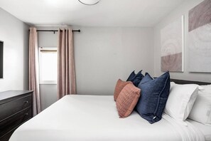 A hotel room with a bed, a dresser, a window with curtains, and artwork on the wall. - The Manta Ray - Spacious Apt, Walk to Mass Ave (Indianapolis)
