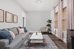 A living room with a grey sofa, a white coffee table, a patterned rug, a beige armchair, and a potted plant. - The Manta Ray - Spacious Apt, Walk to Mass Ave (Indianapolis)