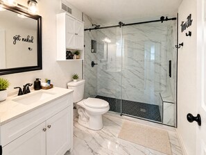 Un baño con tocador blanco, cabina de ducha de vidrio y retrete.