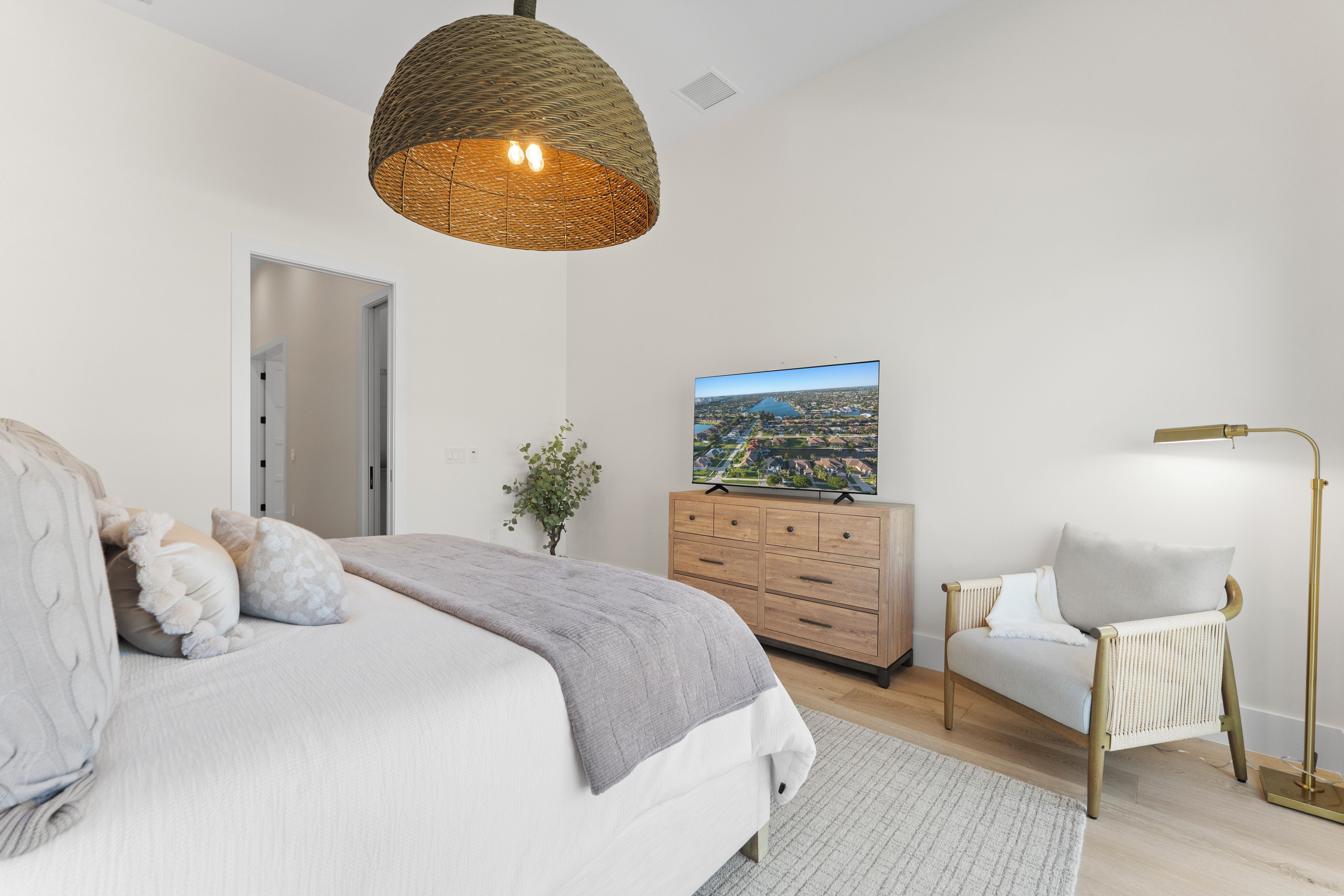 A modern bedroom with a bed, dresser, chair, and a television displaying a cityscape.