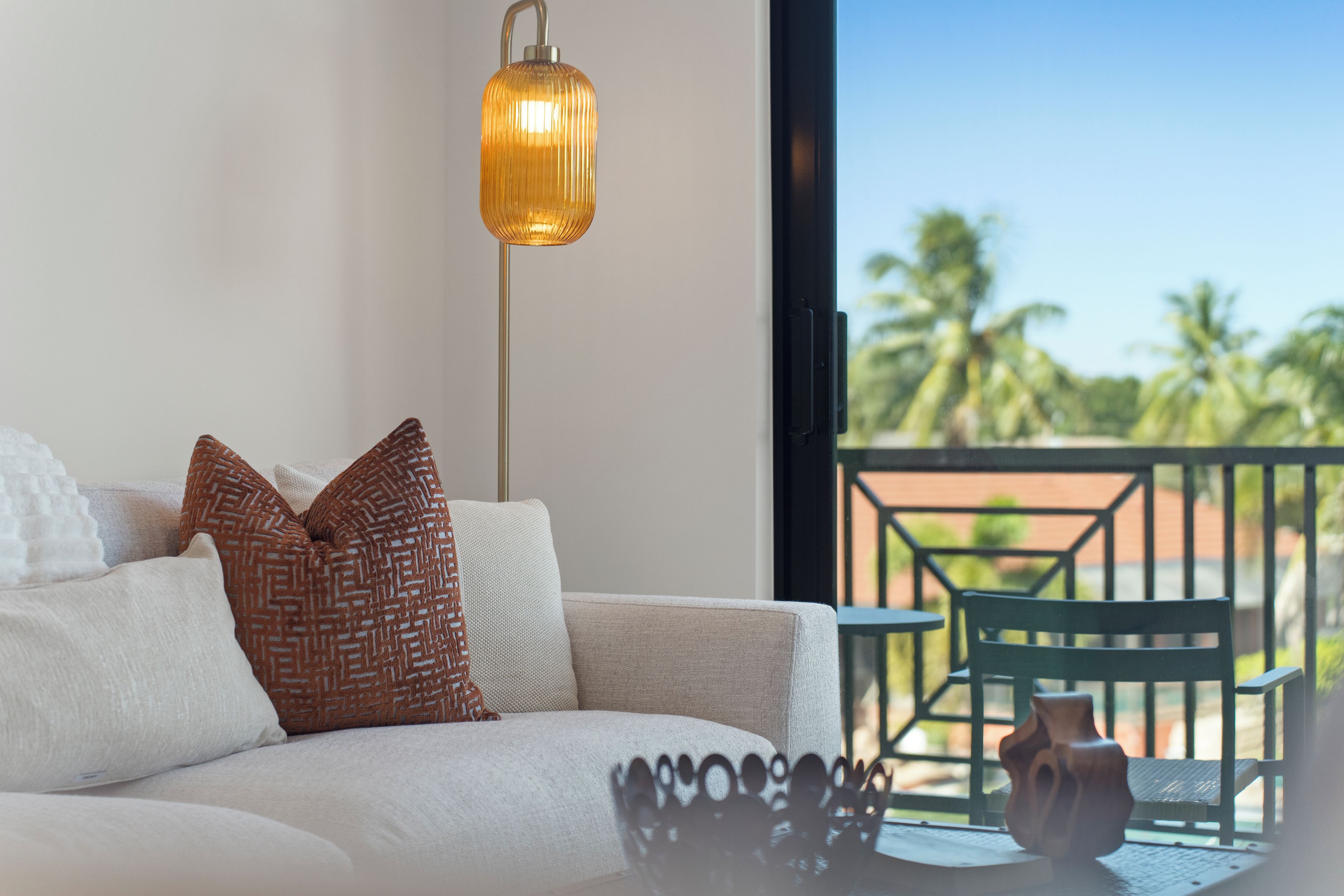 A modern living room with a sofa, patterned pillows, a floor lamp, and a view of the outdoors.