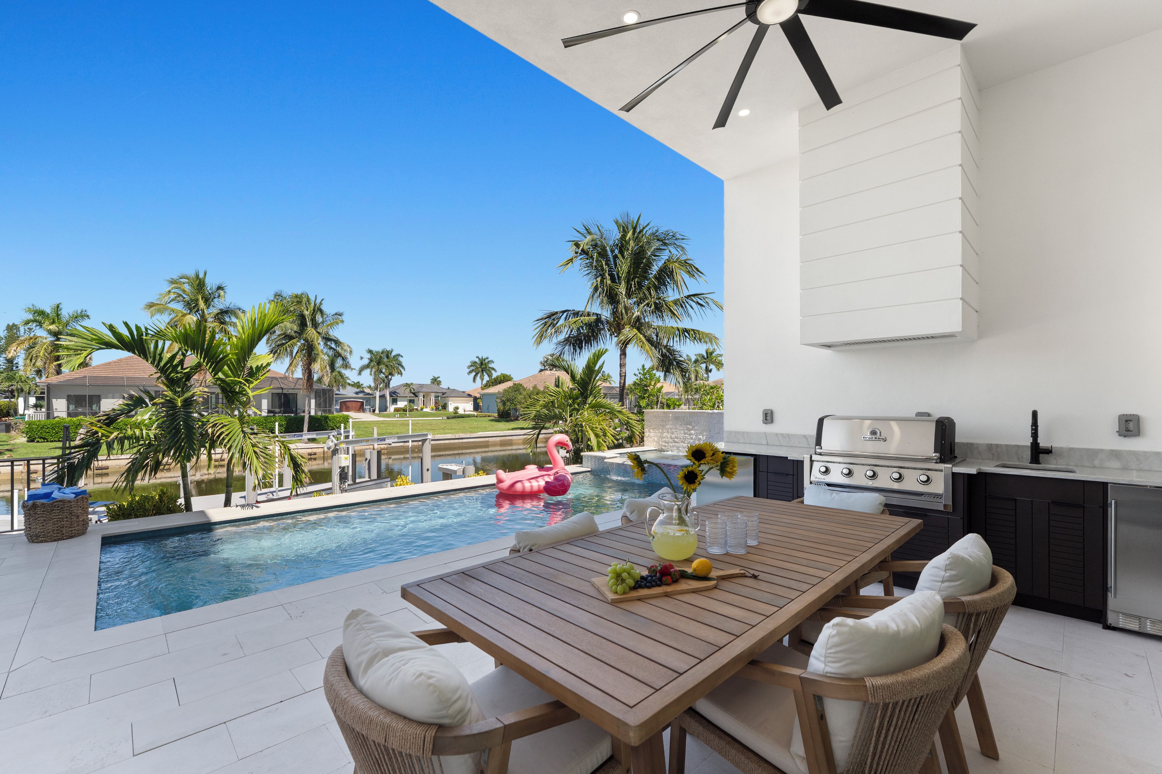 An outdoor pool area with a wooden table, chairs, and a grill.