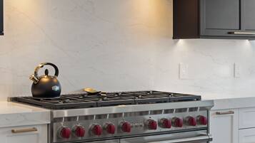 A kitchen with a stainless steel stove, a kettle, and white marble countertops.