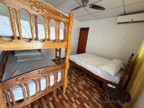 Una habitación con una cama litera, una cama individual, un ventilador de techo, un equipo de aire acondicionado y suelo de madera.