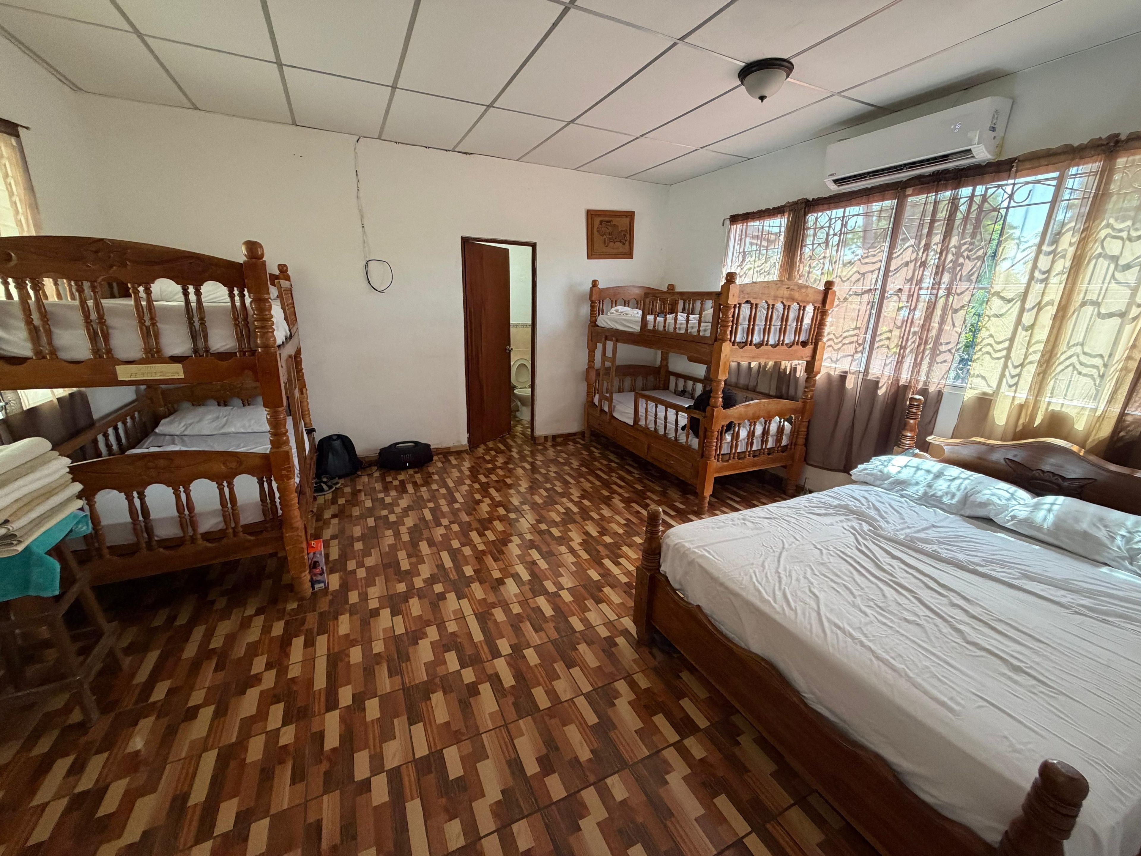 A room with bunk beds, a single bed, a door leading to a bathroom, and a window with curtains.
