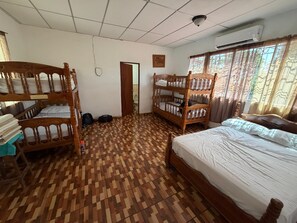 Ein Zimmer mit Etagenbetten, einem Einzelbett, einer Tür zu einem Badezimmer und einem mit Vorhängen versehenen Fenster.