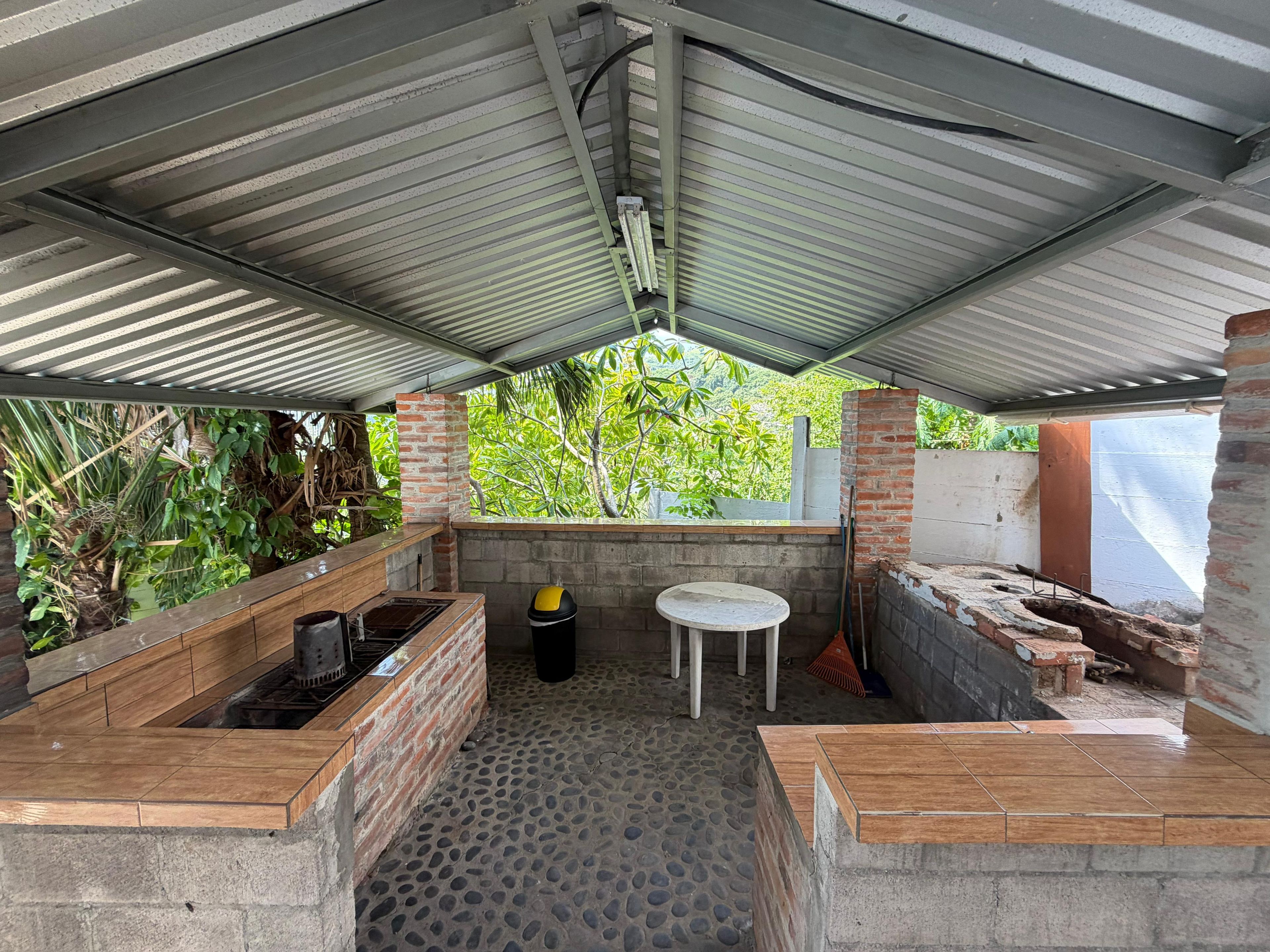 An outdoor kitchen area with a metal roof, a brick counter, and a stone floor.