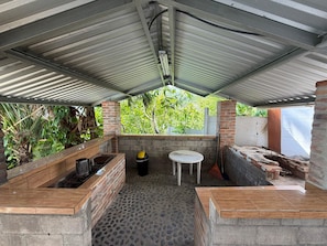 Un área de cocina al aire libre con techo de metal, encimera de ladrillo y suelo de piedra.