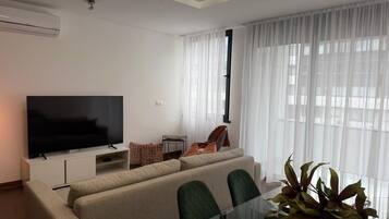 Een moderne woonkamer met een flatscreen televisie, bank, glazen salontafel en een kamerplant.