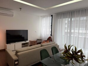 Ein modernes Wohnzimmer mit Flachbildfernseher, Sofa, Glastisch und einem Blumentopf.