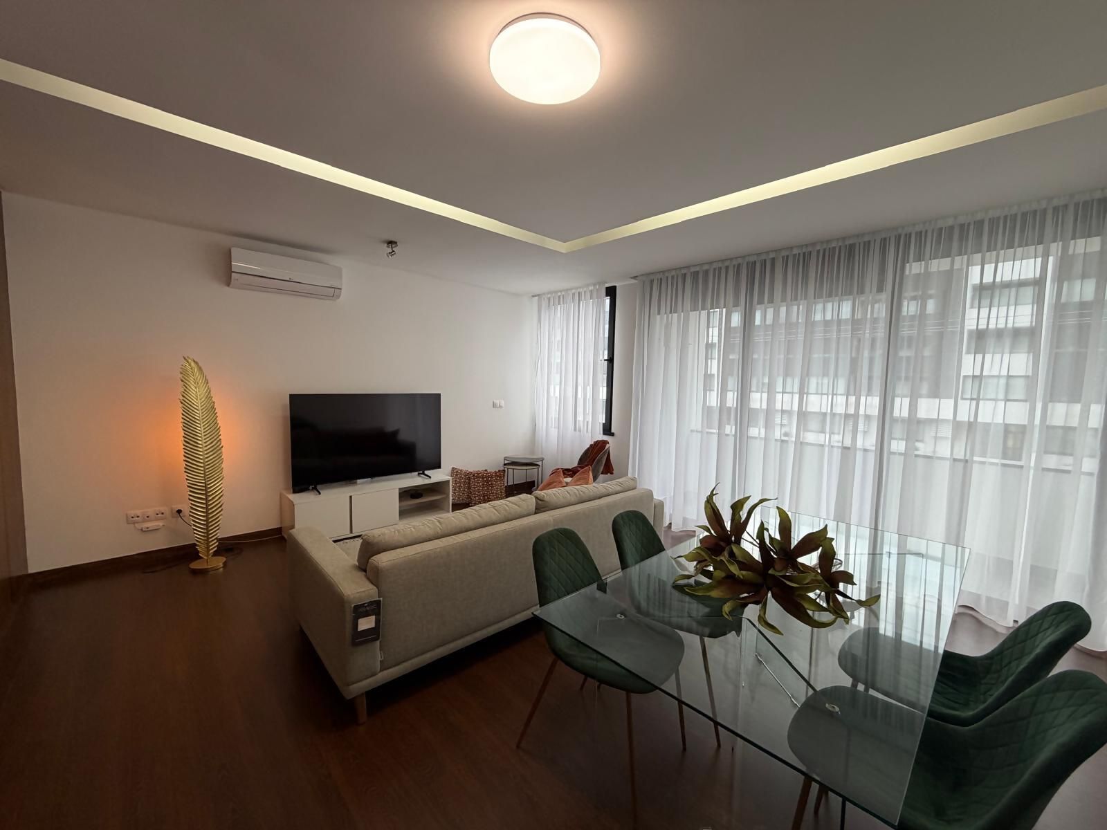 A modern living room with a sofa, a glass dining table, and a flat-screen TV.