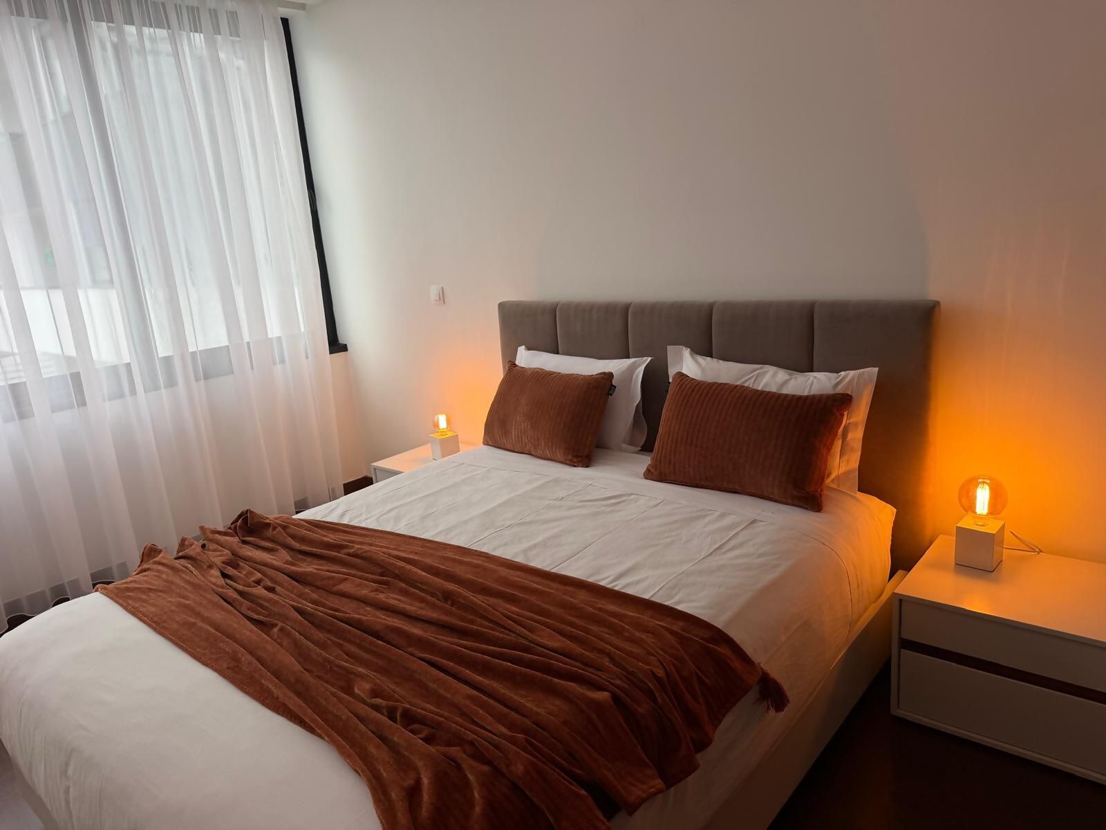 A neatly made bed with a brown blanket, a headboard, and two bedside lamps.