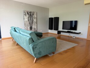 A living room with a teal sofa, a large painting, a flat-screen TV, and a black entertainment unit. - AZORES APARTMENTS PAIM 1NASC (Ponta Delgada)