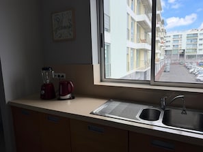 A kitchen with a window view of a parking lot and buildings. - AZORES APARTMENTS PAIM 1NASC (Ponta Delgada)