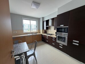 A modern kitchen with a dining table, chairs, a window, and built-in appliances. - AZORES APARTMENTS PAIM 1NASC (Ponta Delgada)