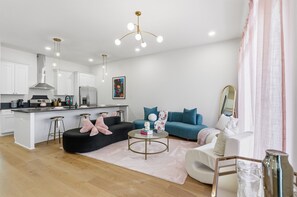 A modern living room with a black sofa, a blue sofa, a round coffee table, and a kitchen area with white cabinets and a stainless steel refrigerator. - Pretty in Pink: Rooftop Hot Tub & Sauna | 4 Ensuite Bedrooms | Sleeps 14 (Nashville)