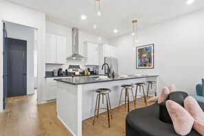 A modern kitchen with white cabinets, a stainless steel range hood, and a central island with bar stools. - Pretty in Pink: Rooftop Hot Tub & Sauna | 4 Ensuite Bedrooms | Sleeps 14 (Nashville)