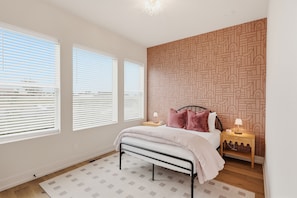 A bedroom with a bed, bedside tables, a patterned wall, and large windows with blinds. - Pretty in Pink: Rooftop Hot Tub & Sauna | 4 Ensuite Bedrooms | Sleeps 14 (Nashville)