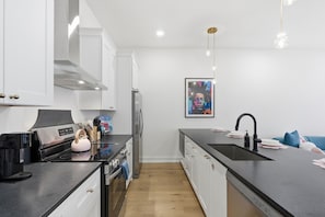 A modern kitchen with white cabinets, a stainless steel refrigerator, a black countertop, and a single pendant light. - Pretty in Pink: Rooftop Hot Tub & Sauna | 4 Ensuite Bedrooms | Sleeps 14 (Nashville)