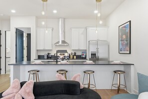 A modern kitchen with white cabinets, stainless steel appliances, and a central island with bar stools. - Pretty in Pink: Rooftop Hot Tub & Sauna | 4 Ensuite Bedrooms | Sleeps 14 (Nashville)