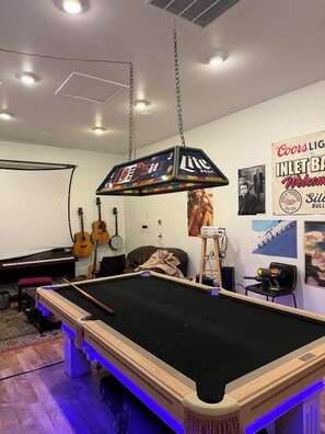 Una taula de bitlles amb un turmell, un piano, guitarres i un cartell de Coors Light en una habitació de parets blanques i terres de fusta.
