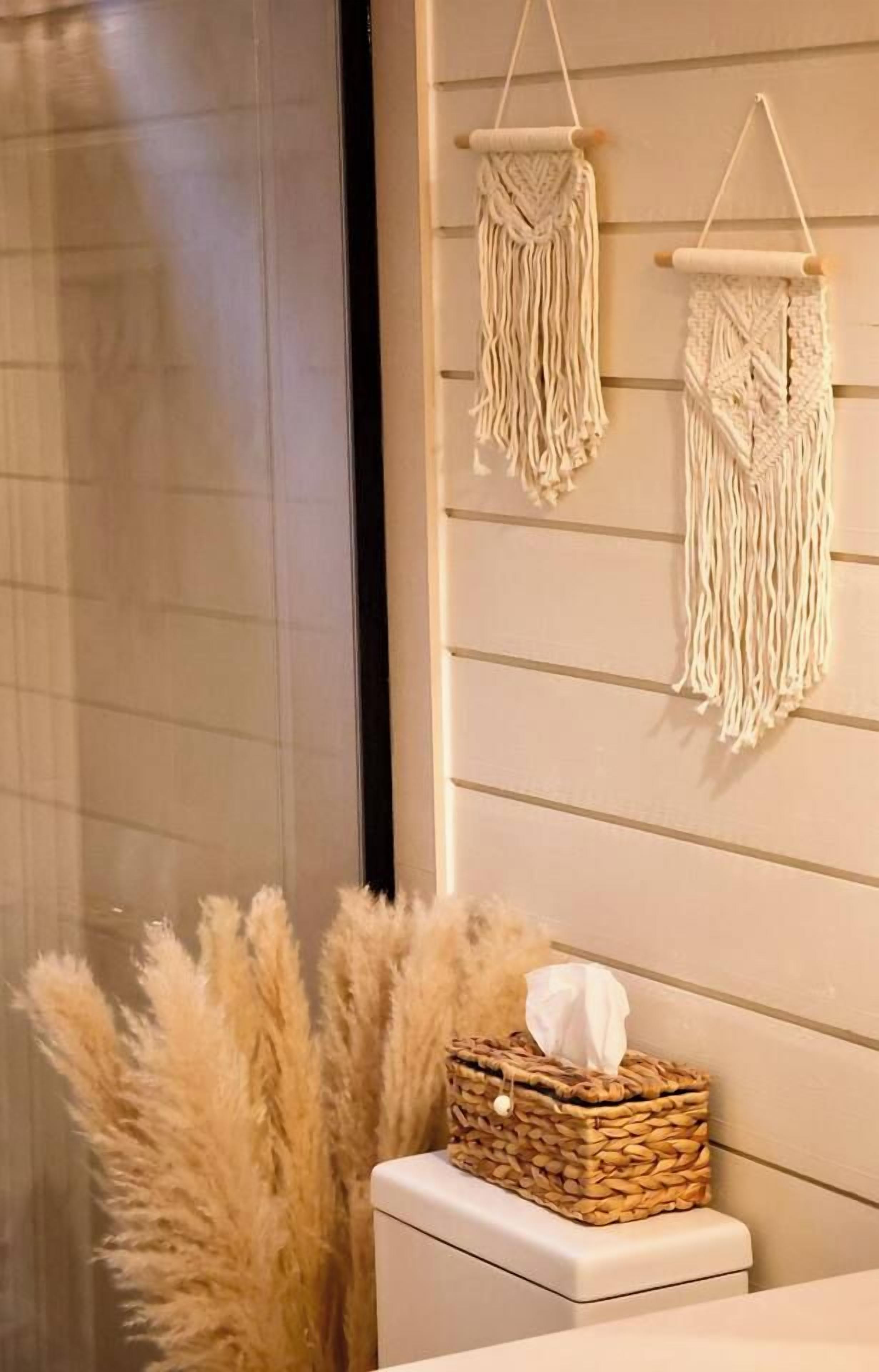 A bathroom with a toilet, a tissue box on the edge, and two macramé wall hangings.